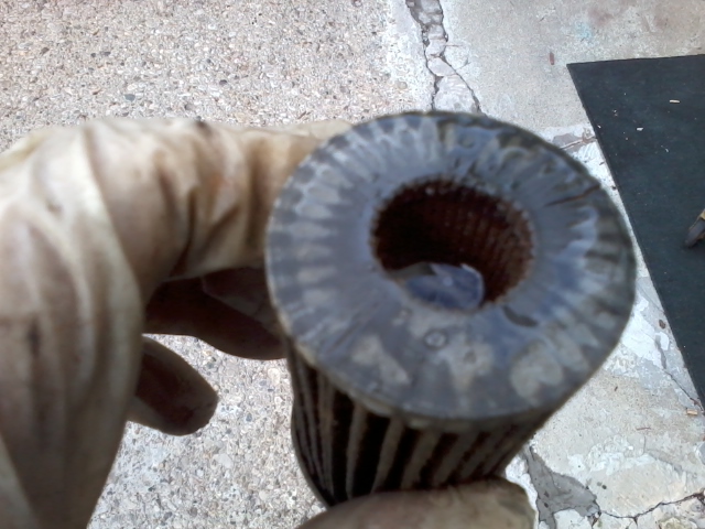 Close-up of a used oil filter held by a gloved hand.