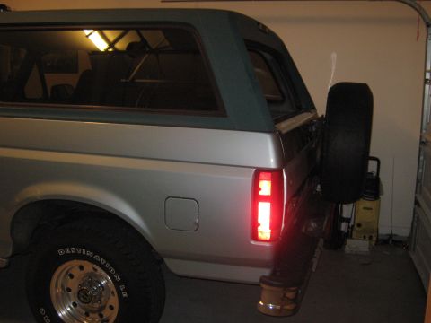 1996 Ford Bronco - The rear quarter panel and taillight of a silver Ford Bronco with a green removable top are visible.