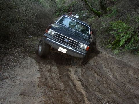 1989 Ford Bronco - A black 1987 Ford Bronco tackles a challenging muddy off-road course, demonstrating its capabilities.