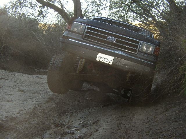 Dark Ford SUV tilted on a steep dirt off-road trail with a raised mud-terrain tire