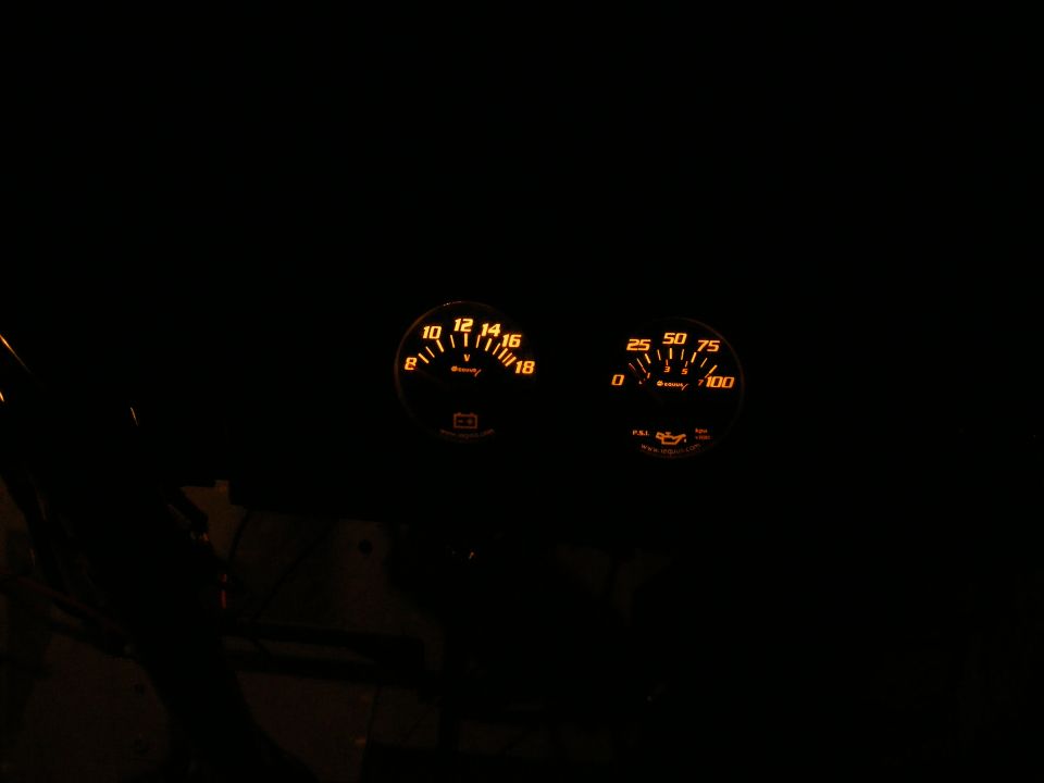 Two illuminated gauges in a dark vehicle interior: a voltmeter and an oil pressure gauge