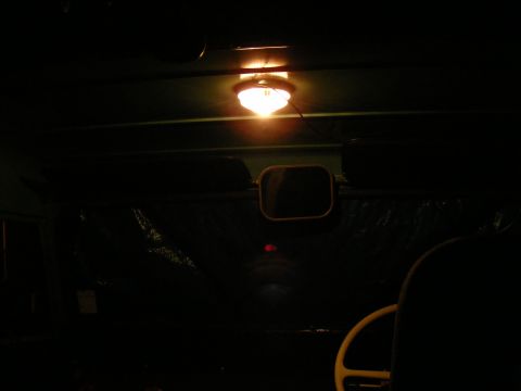 Interior view of a vehicle with a dome light on, a side mirror, and part of a steering wheel visible