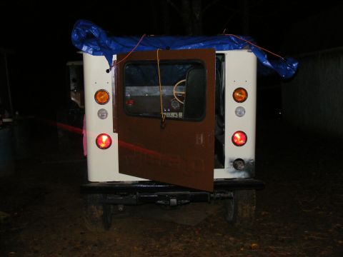 Rear view of a white off-road vehicle with brown door open, blue tarp on roof