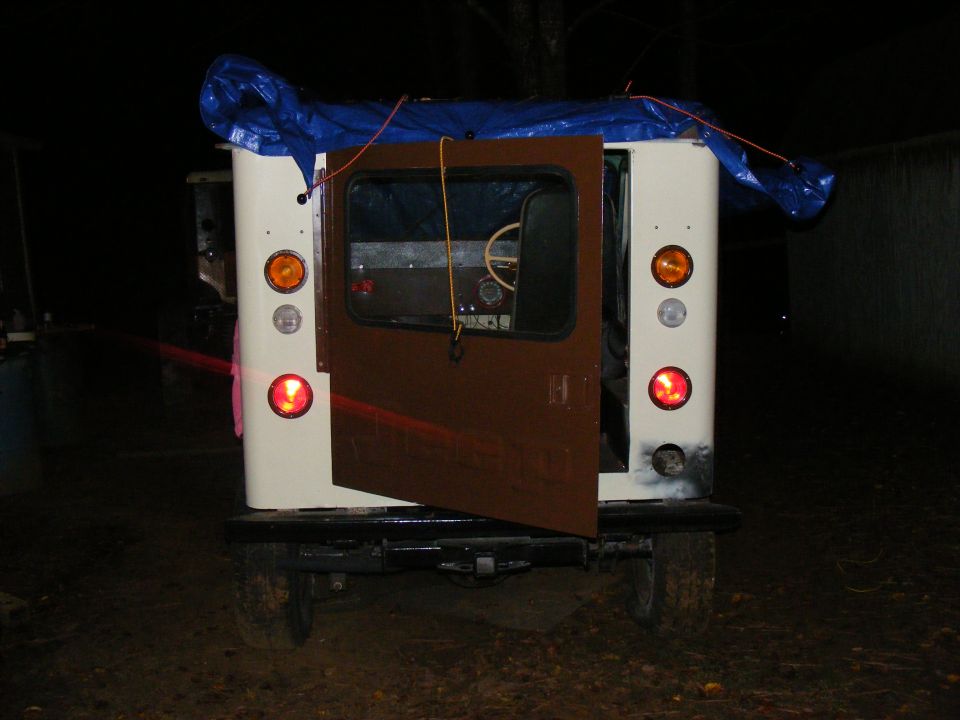 Rear view of a white off-road vehicle with brown door open, blue tarp on roof