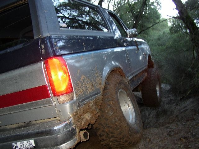 Muddy gray Ford Bronco rear quarter with off-road tires on a wet trail