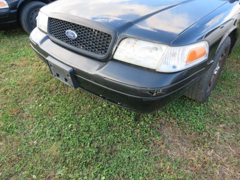1991 Ford LTD Crown Victoria - Front end of a black Ford Crown Victoria showing the grille and bumper damage. Another car is parked nearby.