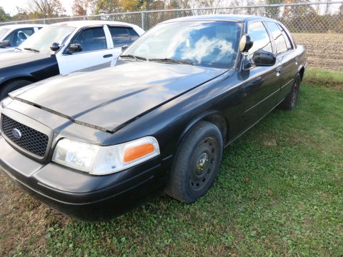 1991 Ford LTD Crown Victoria - A black police car is parked in a grassy lot next to other vehicles. The hood of the police car is open.