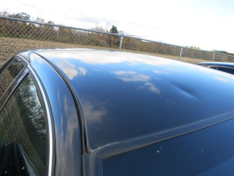 1991 Ford LTD Crown Victoria - The reflection of clouds on the dark car roof is interrupted by a significant dent.