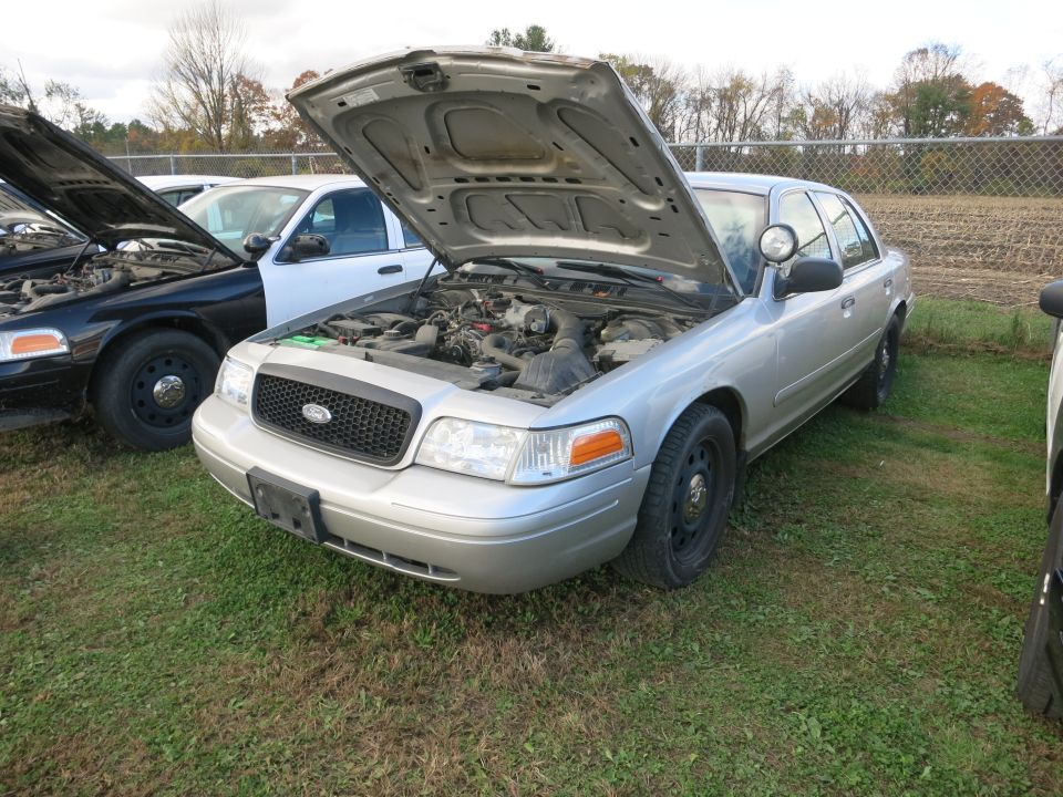 Silver Ford Crown Victoria police car with hood open, parked next to a black police car
