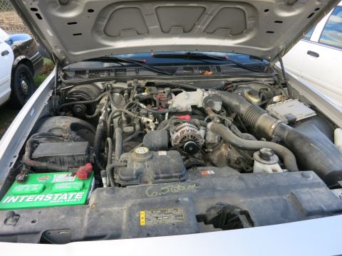 1991 Ford LTD Crown Victoria - The engine compartment of a vehicle, with the hood open, revealing the engine components and a green Interstate battery.
