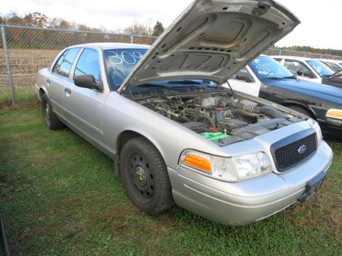 1991 Ford LTD Crown Victoria - Silver sedan with hood open, parked on grass with a fence and field behind it.