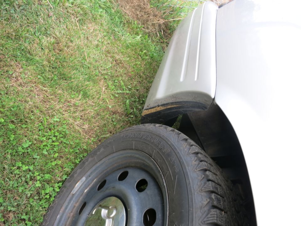 Close-up of a car's front fender and tire. The fender has vertical trim lines