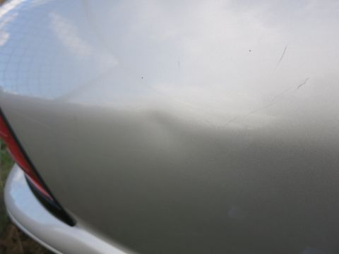 1991 Ford LTD Crown Victoria - Close-up of a silver car fender showing a noticeable dent and several scratches.