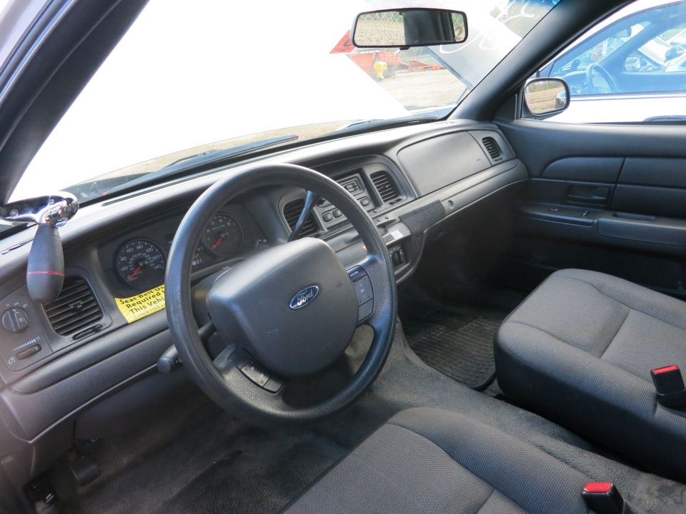 Interior view of a Ford Crown Victoria with a yellow 'Seat Belt Required' sticker on the dashboard