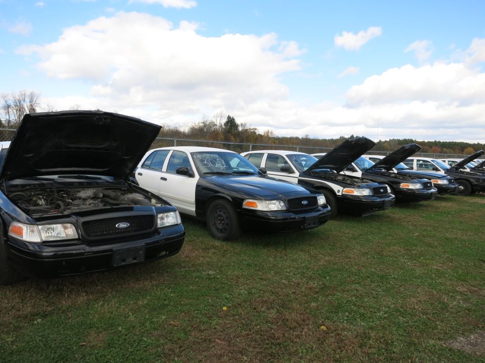 Black Ford Crown Victoria with hood open, parked in a lot with other similar vehicles