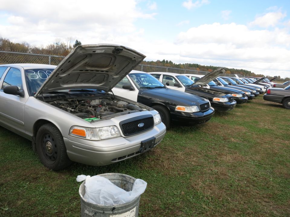 Several Ford Crown Victoria police cars lined up, hoods open. One silver car in foreground