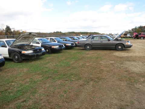 1991 Ford LTD Crown Victoria - Several Ford Crown Victoria sedans are parked in a grassy lot under a cloudy sky.