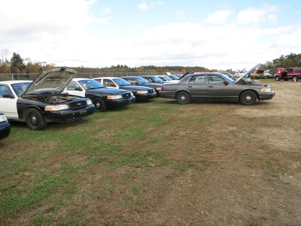 Dark gray Ford Crown Victoria sedan parked in a lot with hoods open on other vehicles