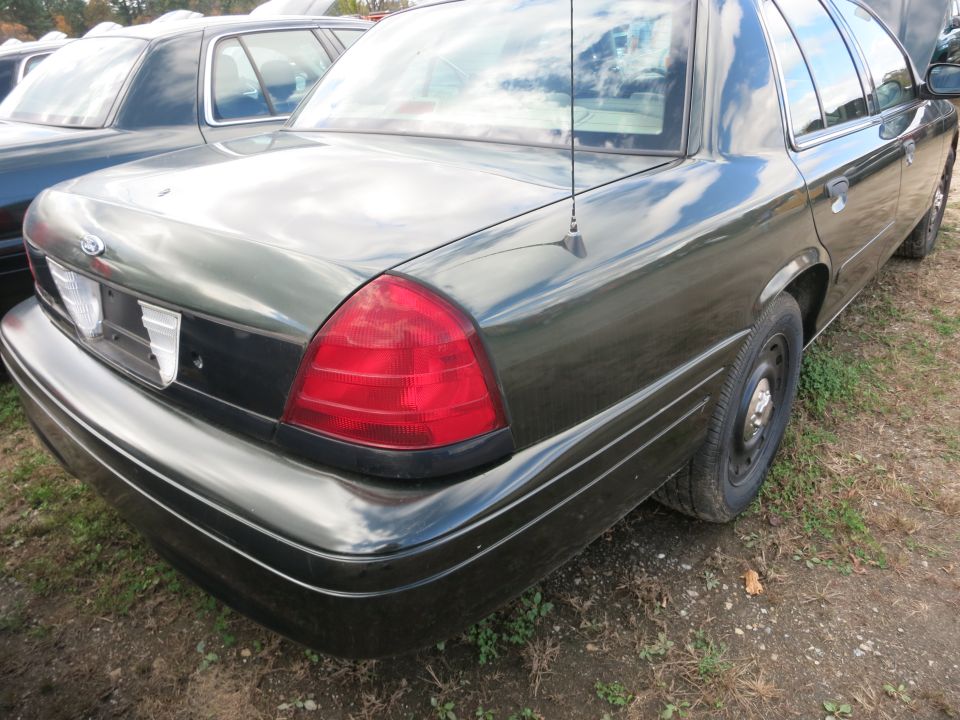Rear quarter view of a dark green sedan, parked next to another vehicle. Shows taillight, bumper, and wheel