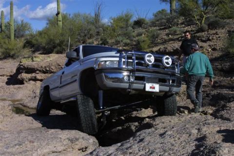 1994 Ford Bronco - Dodge Ram pickup truck driving over rocks in a desert landscape.