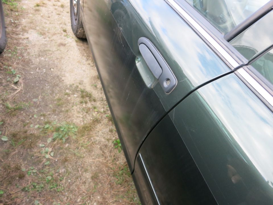 Side view of a green car's door and front wheel. The door has scratches and a black door handle
