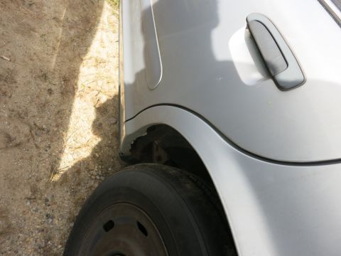 1991 Ford LTD Crown Victoria - Close-up of a silver car's rear fender and wheel, showing damage to the wheel well opening.
