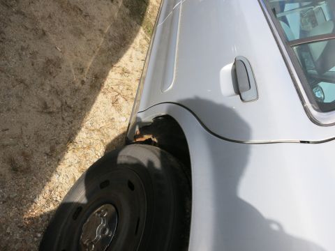 1991 Ford LTD Crown Victoria - The rear wheel well of a silver sedan shows some rust and damage.