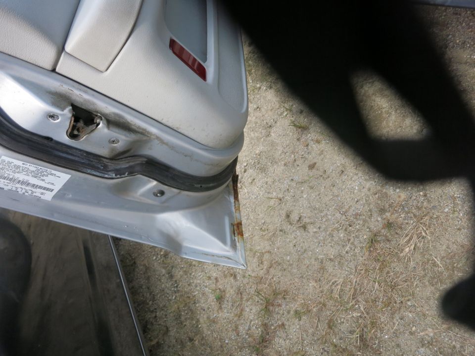 Silver car door interior with visible rust on the frame and a sticker on the door jamb