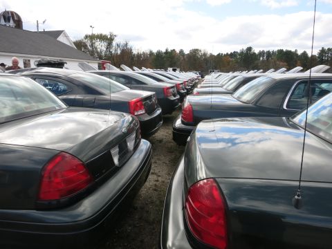 1991 Ford LTD Crown Victoria - A large group of dark-colored sedans are parked in rows under a cloudy sky.