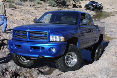 1994 Ford Bronco - A blue 1994 Dodge Ram pickup truck navigates rocky terrain, with another black truck visible in the background.