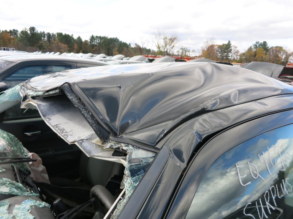 Close-up of a crushed sedan roof and broken glass at a surplus lot