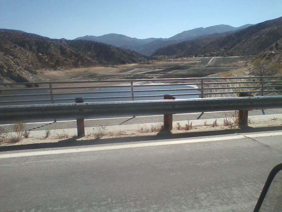 Bridge railing overlooking a body of water with dry hills and mountains in the background.