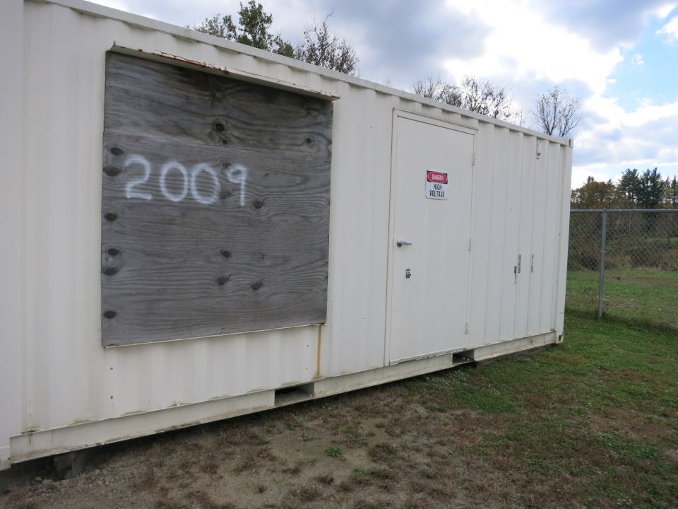 White shipping container generator enclosure marked 2009 in a field