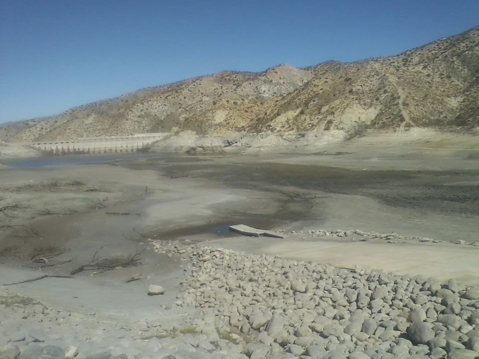 Dry lakebed with a dam and a small wooden dock.