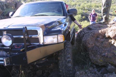 1994 Ford Bronco - A black pickup truck is carefully driven over rough terrain, with a large rock obstructing its path.