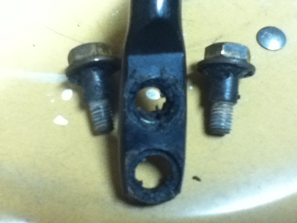 Two bolts and a metal bracket with two holes on a yellow surface.
