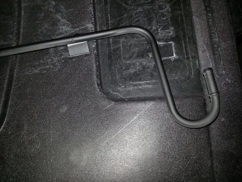 1994 Ford Bronco - Photograph of a black bent metal bar with a retaining clip on a textured truck bed liner.