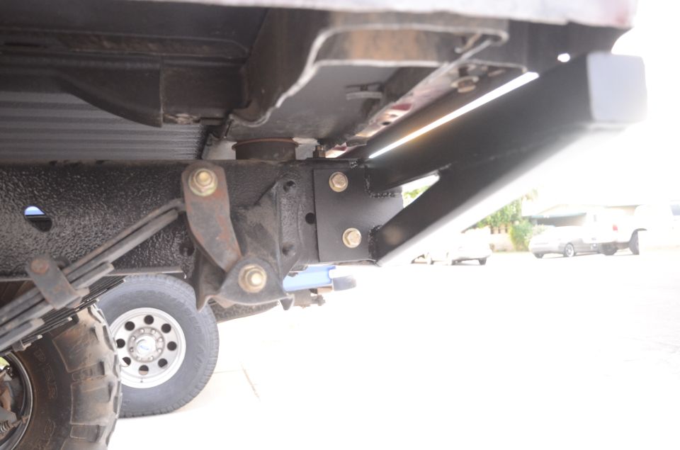 Underside of a vehicle showing frame modification, leaf springs, and tire.