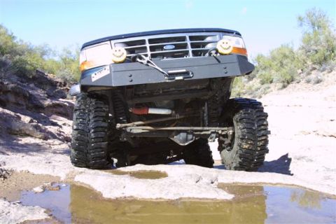 1994 Ford Bronco - This modified Ford Bronco navigates a rocky desert terrain with large off-road tires.