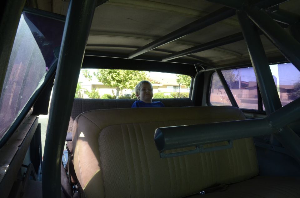 Interior of a 1979 Ford Bronco with a roll cage and a boy sitting in the back seat.