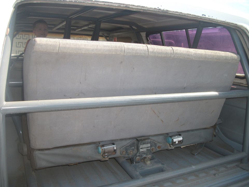 Interior view of a vehicle with a grey bench seat and roll cage.