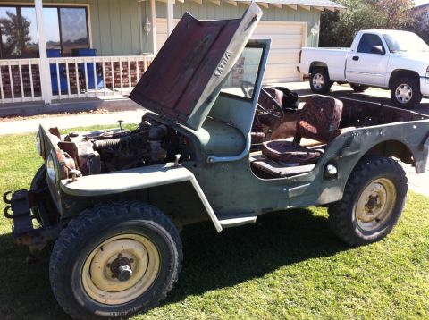 1946 Jeep Willys - A vintage olive green Jeep CJ-5 with its hood open sits on a grassy lawn in front of a house. The Jeep has a weathered appearance and its i…