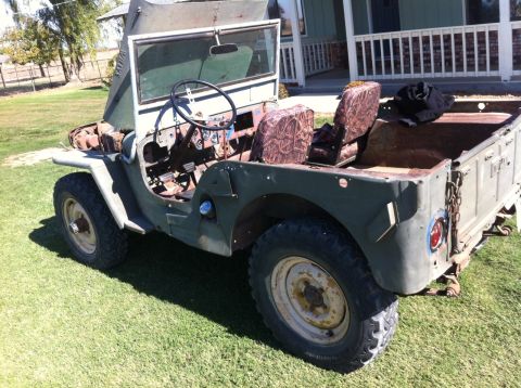 1946 Jeep Willys - A weathered olive green Jeep is parked on a grassy lawn in front of a house with a white porch railing. The hood is propped open, revealing…