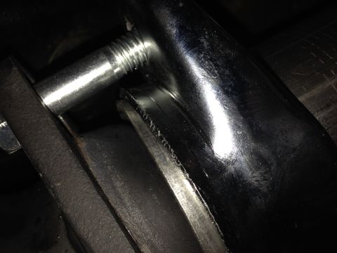 1992 Ford F-150 - Tight low-light macro of a zinc-plated threaded stud or bolt passing through a black-painted bracket alongside a shiny curved steel tube, w…