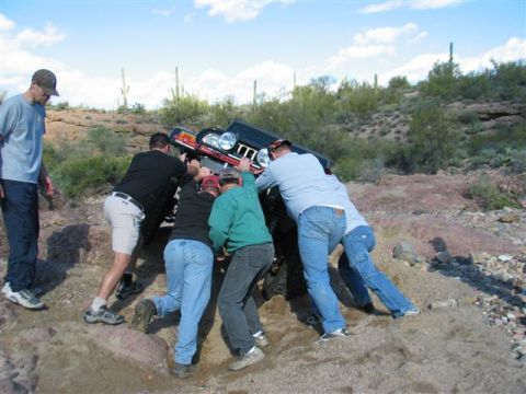 1994 Ford Bronco - Men push a stuck SUV on a rocky desert trail under a blue sky with scattered clouds.