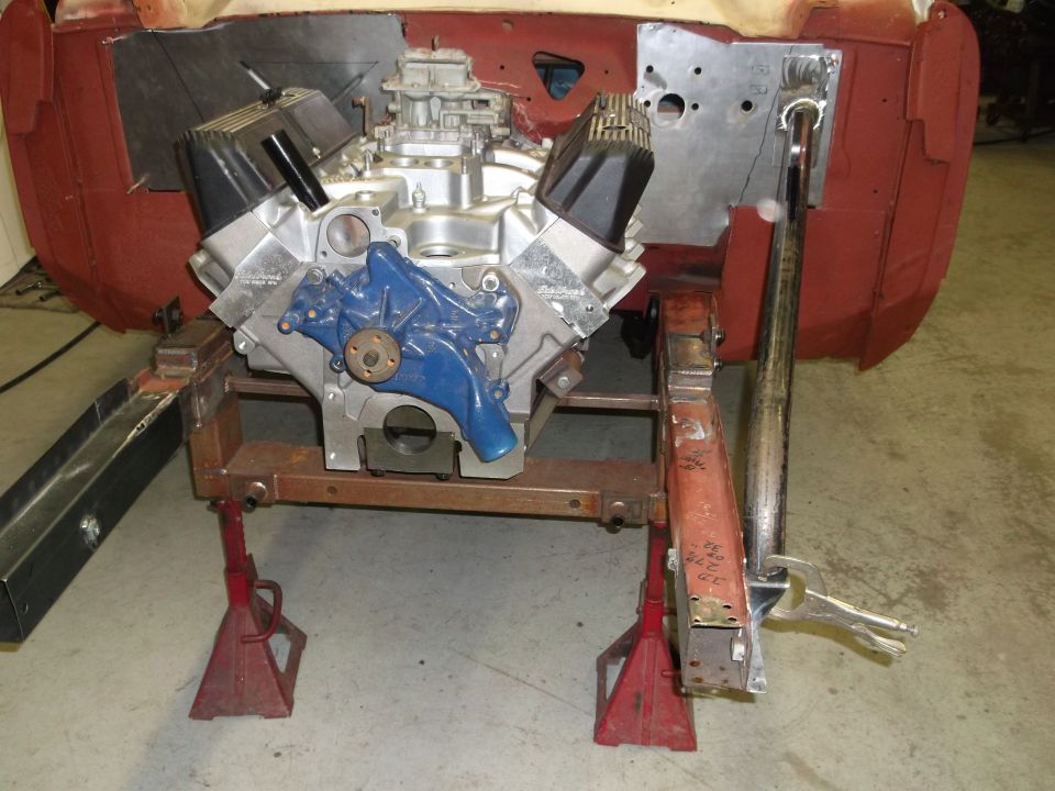 Engine assembly with blue water pump and black valve covers on red jack stands, undergoing repair
