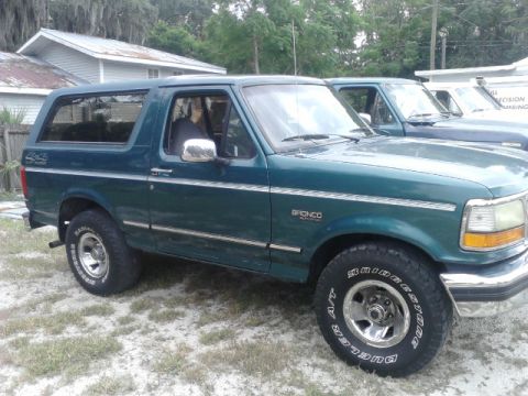 1996 Ford Bronco - A green Ford Bronco is parked outside, with another vehicle behind it. The Bronco's side and front quarter are visible.
