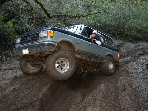 1989 Ford Bronco - This two-tone Ford Bronco navigates a challenging muddy trail, demonstrating its off-road capabilities.
