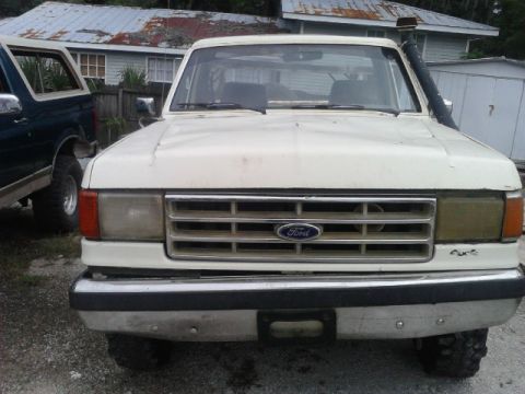 1988 Ford Bronco - Two Ford Broncos are parked outdoors, one white and one dark blue, with a house in the background.