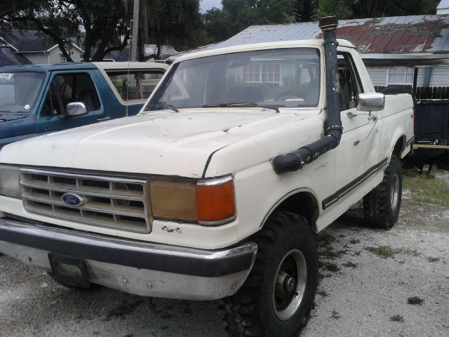 White Ford Bronco with snorkel intake, parked next to a blue SUV